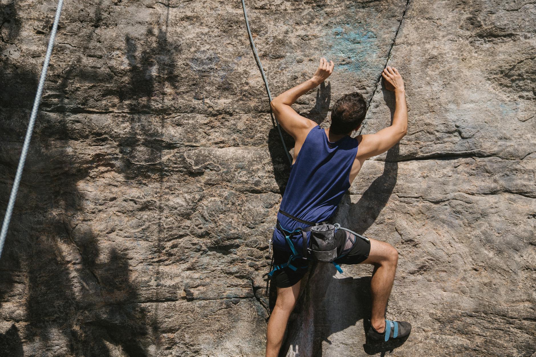 Determined man climbing a rock wall with safety harness and ropes, showcasing adventure and strength.