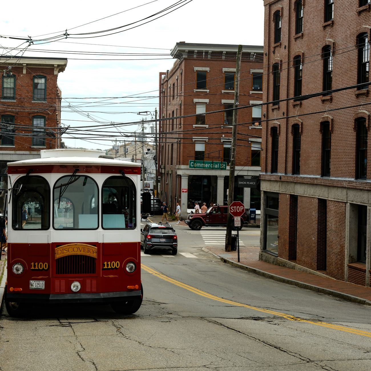 Red vintage trolley passing through a historic city street lined with brick buildings.