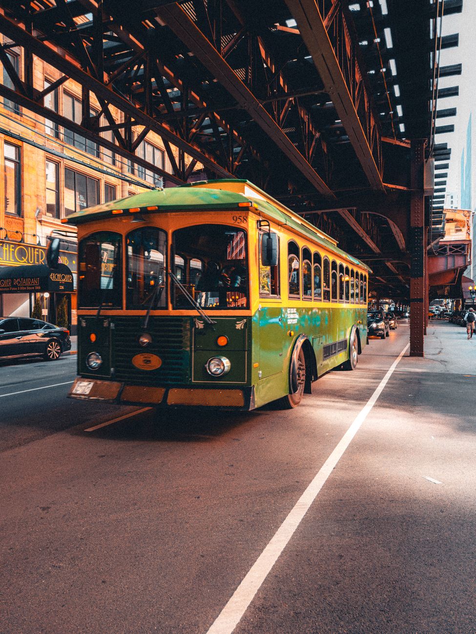 A classic green trolley under a Chicago elevated track, showcasing urban charm.