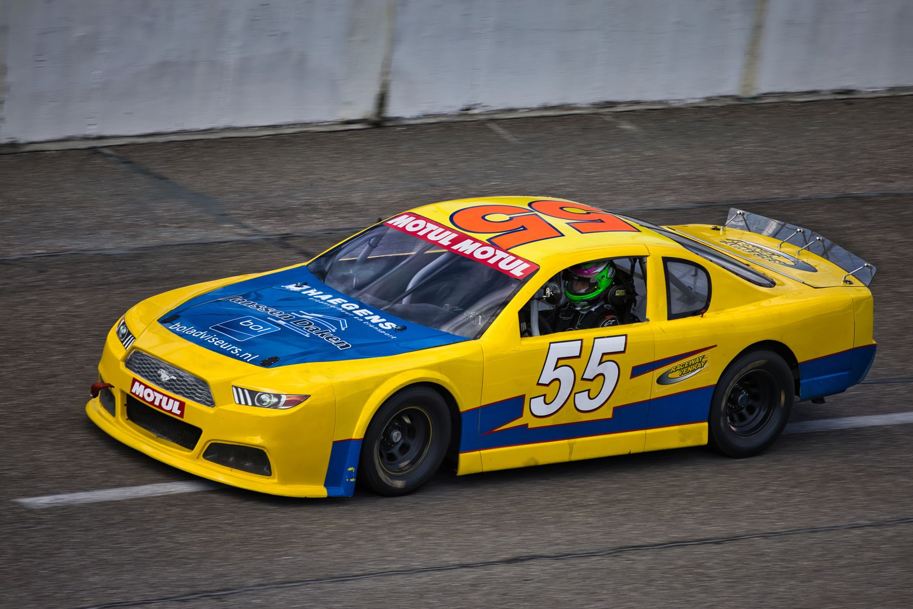 Yellow race car with number 55 speeding on asphalt track during a motorsport event.